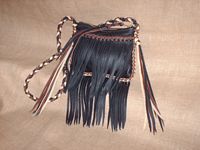  This small Black leather purse has fringe that hangs from its front pocket and from the bottom of the bag. It's about 8" wide and 7" high. It has a large brass zipper closure. The seams, edges, and round strap with tassels are all braided with three colors of leather in various locations using 1/4" wide lace that is cut from the same material the purse is made with - 4 oz. moccasin cowhide. 